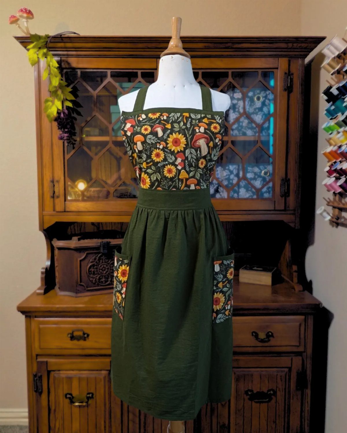 Green garden apron with floral and mushroom patterns on a white mannequin torso.