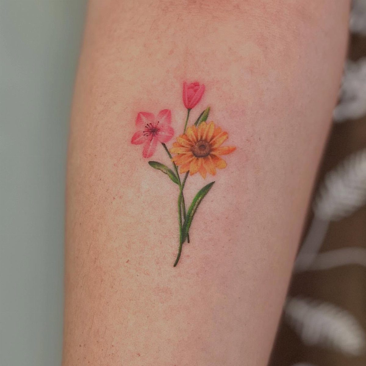 Floral tattoo on a forearm featuring pink, yellow, and red spring flowers.