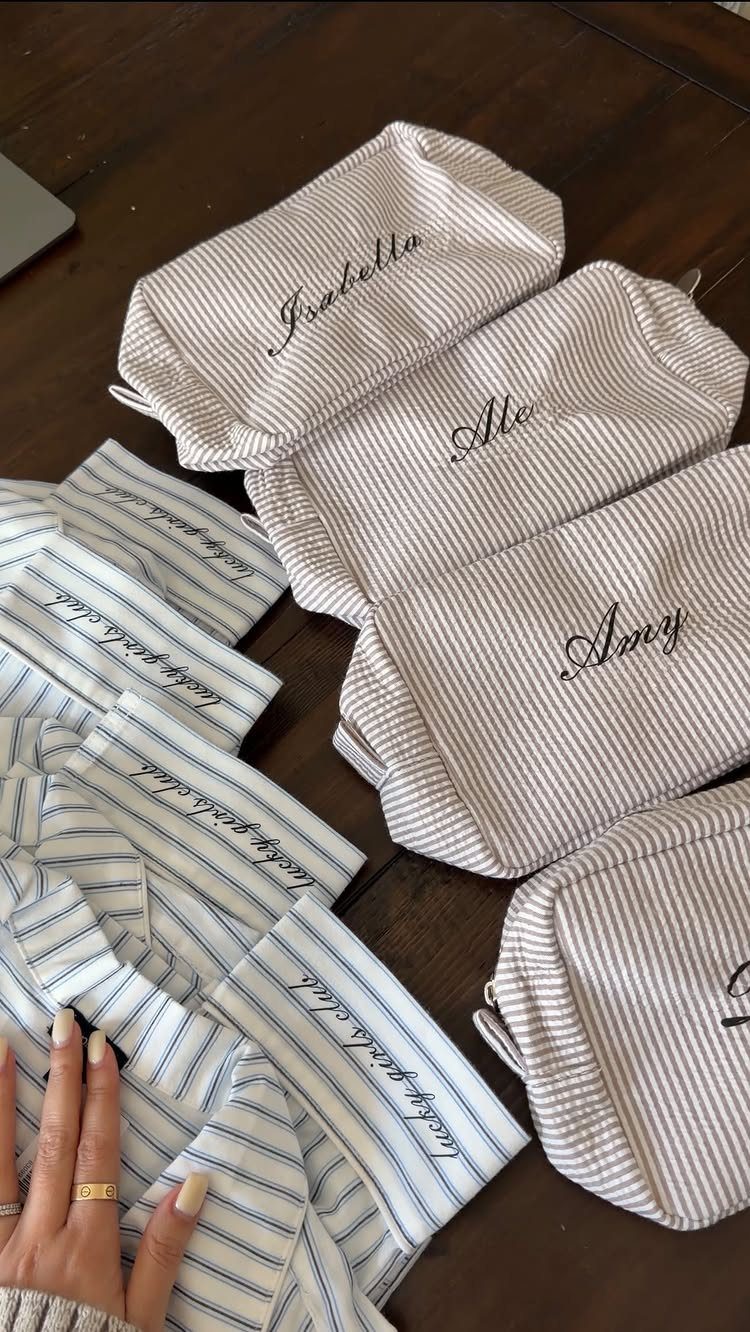 Striped fabric pouches with embroidered names and phrases on a dark wooden table.
