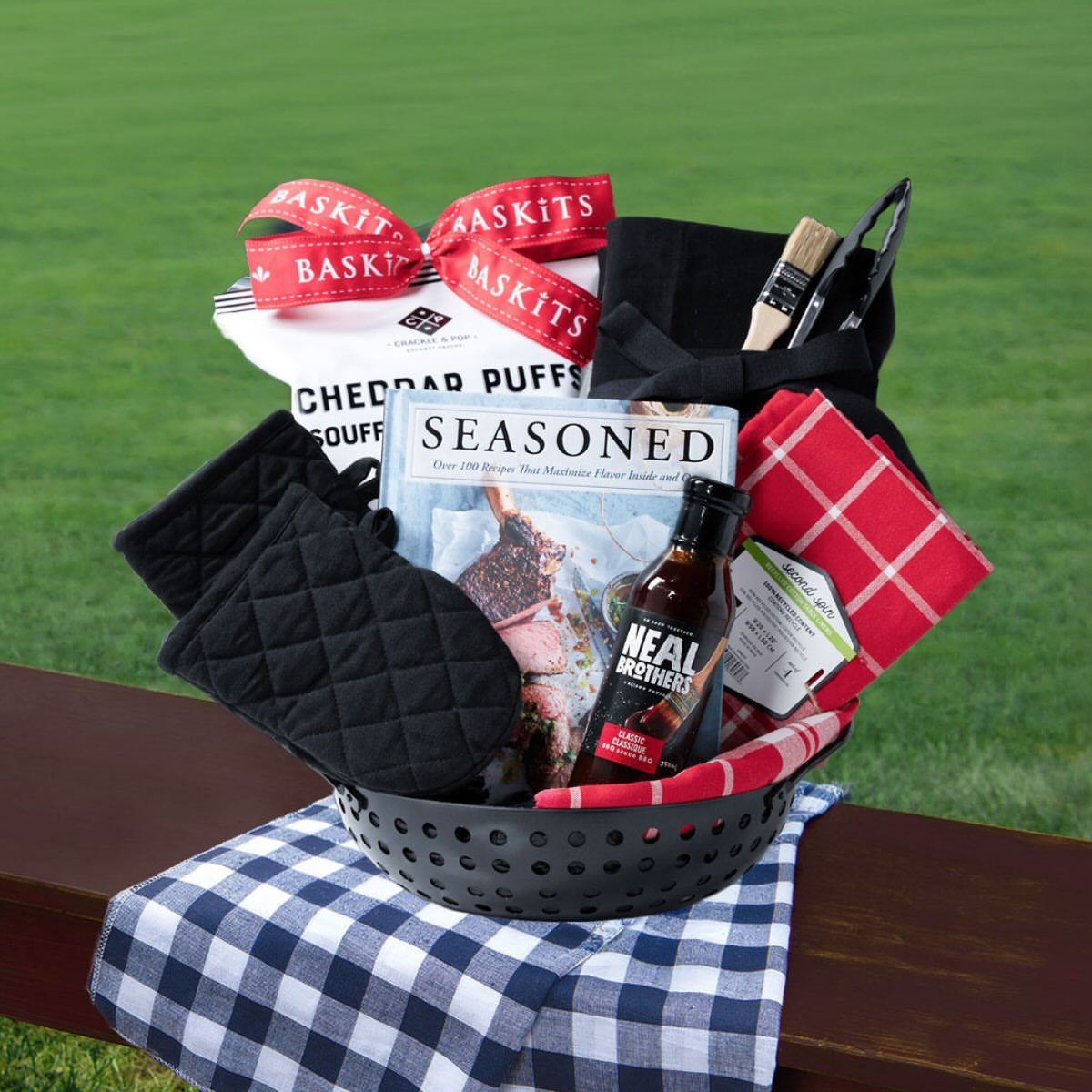 BBQ gift basket with sauce, cookbook, and oven mitts on a wooden rail
