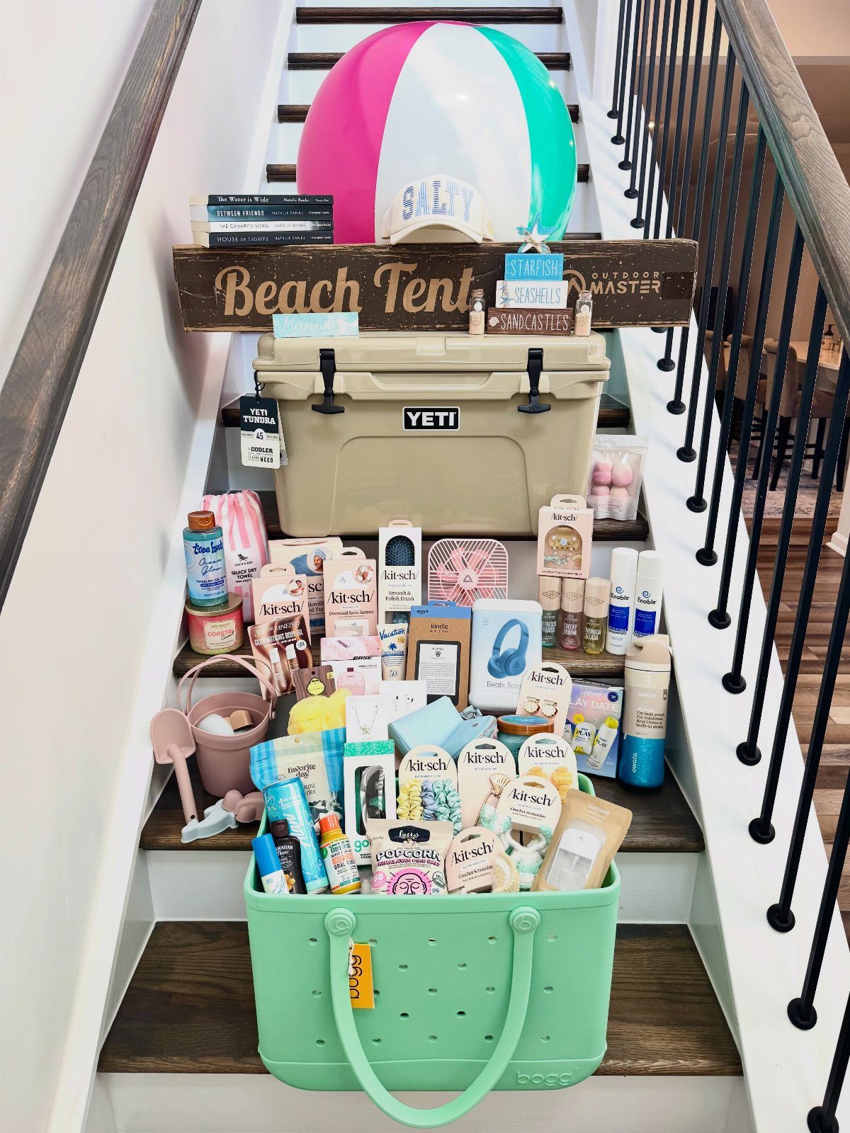 Mint green basket filled with beach essentials next to a Yeti cooler and beach ball.