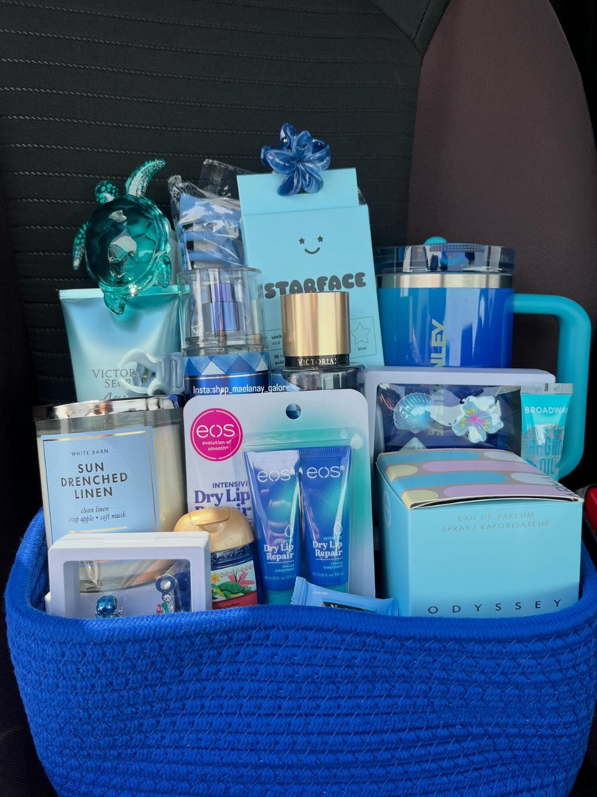 Blue woven gift basket filled with blue themed skincare, candles, and a turtle figurine.