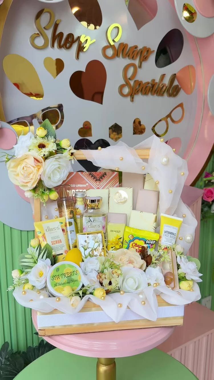 Wooden gift basket with skincare products, soaps, and white flowers on pink pedestal