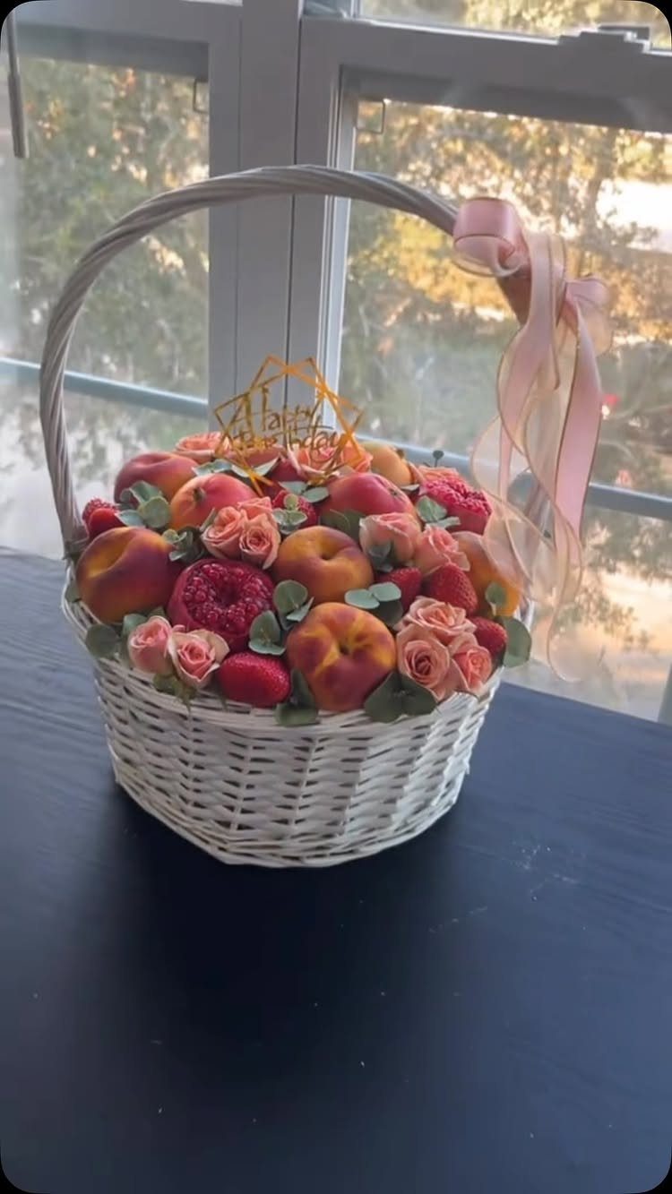 White wicker basket filled with fresh apples, peaches, and pink roses with birthday topper.