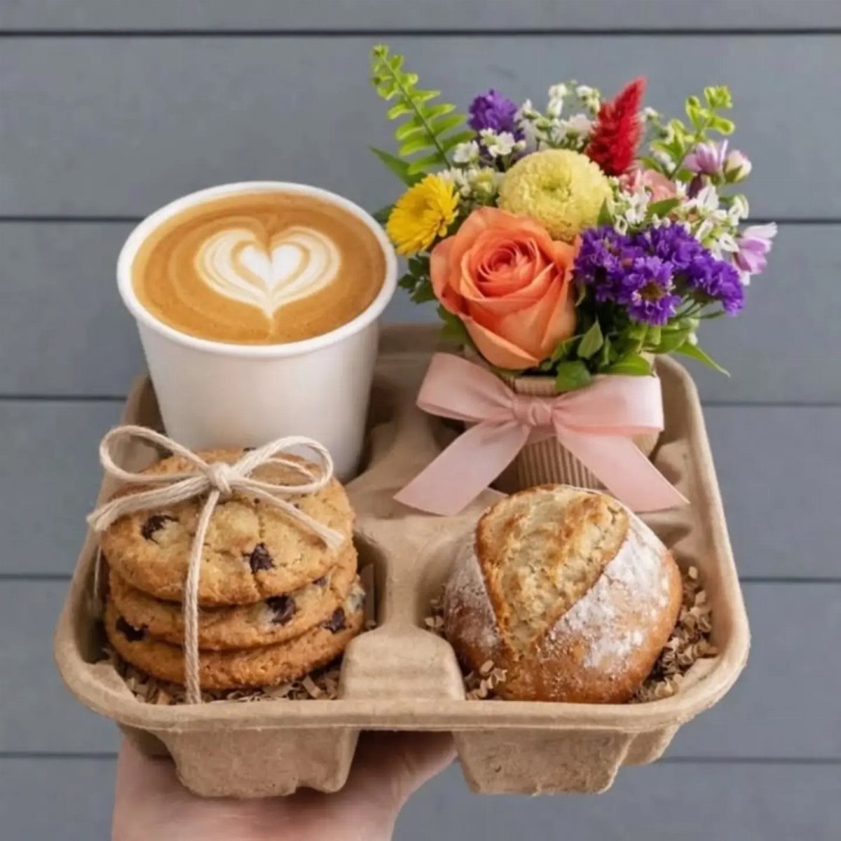 Coffee latte, chocolate chip cookies, a muffin, and colorful flowers in a tray.