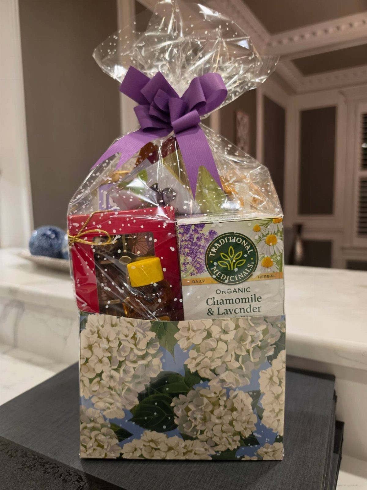 Tea gift basket wrapped in cellophane with a purple bow and floral box.