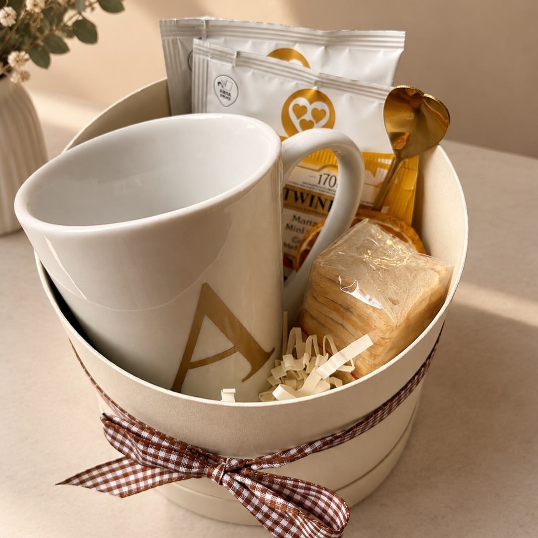 White gift basket with a gold letter A mug, tea, and checkered ribbon.