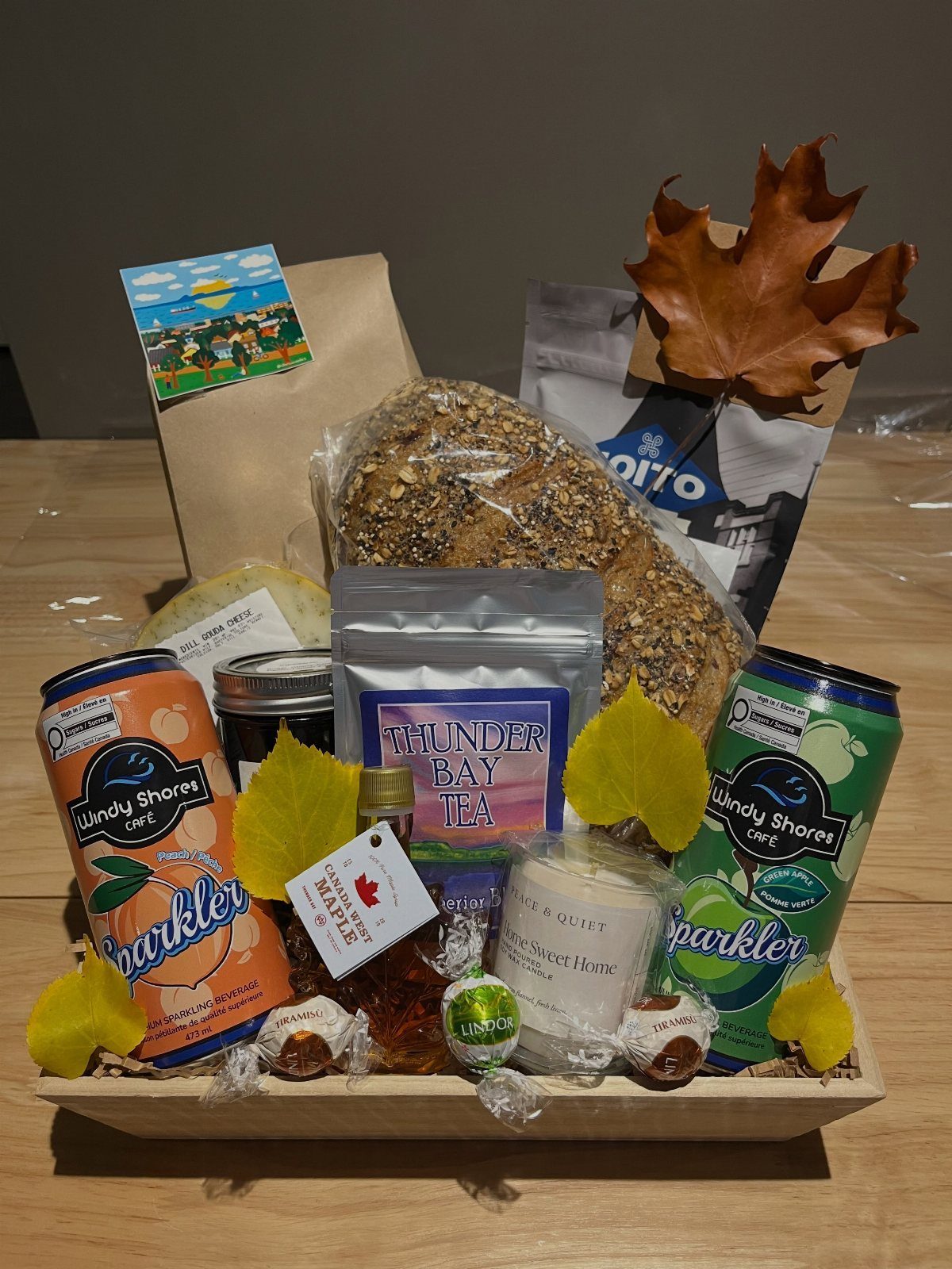 Wooden gift tray with tea, sparkling drinks, bread, and autumn leaf decorations.
