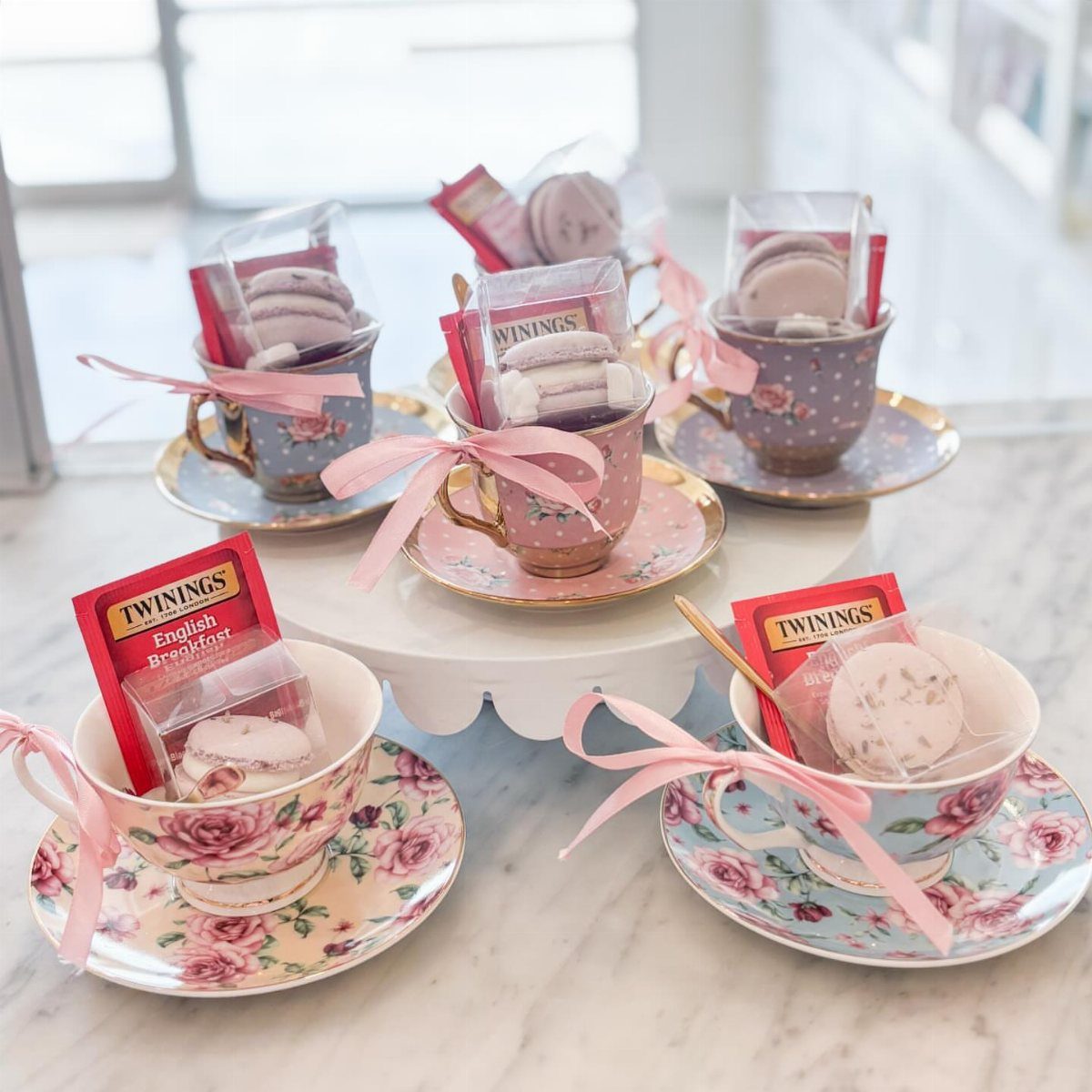 Floral teacups filled with tea bags and macarons tied with pink ribbons