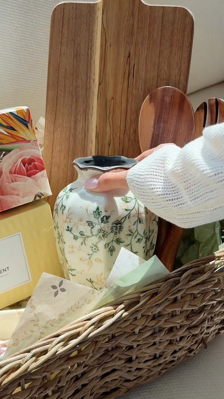 Floral ceramic teapot and wooden kitchenware arranged in a woven wicker gift basket