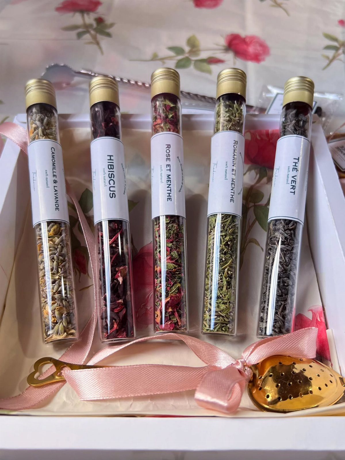 Five glass tubes of loose leaf tea in a white gift box with ribbon.