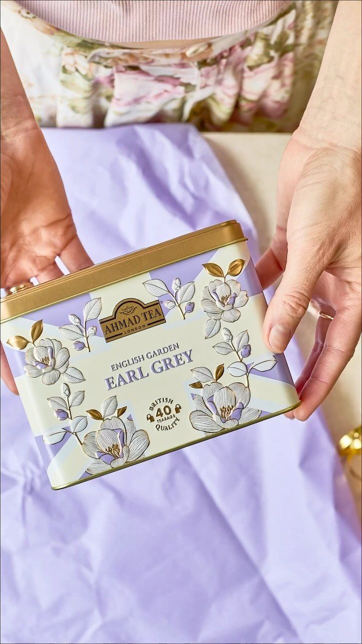 Hands holding a floral Ahmad Tea Earl Grey tin over purple tissue paper