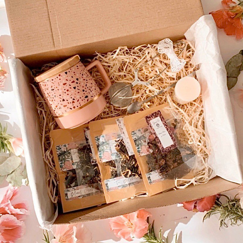 Tea gift box with loose leaf tea packets, pink speckled mug, and strainer.