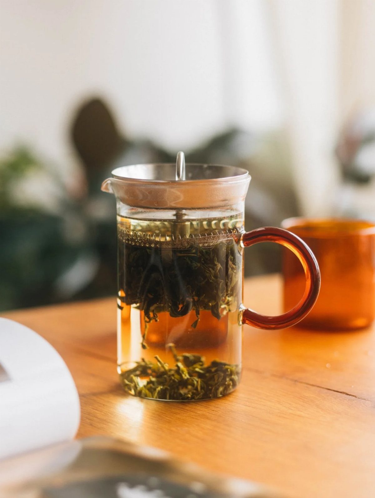 Glass tea steeper with loose leaf tea steeping inside on a wooden table