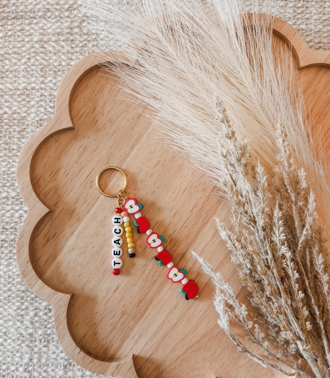 7 Thanksgiving Teacher Gifts for a Heartfelt Thank-You 7 Beaded keychain spelling TEACH on a wooden tray with dried pampas grass.