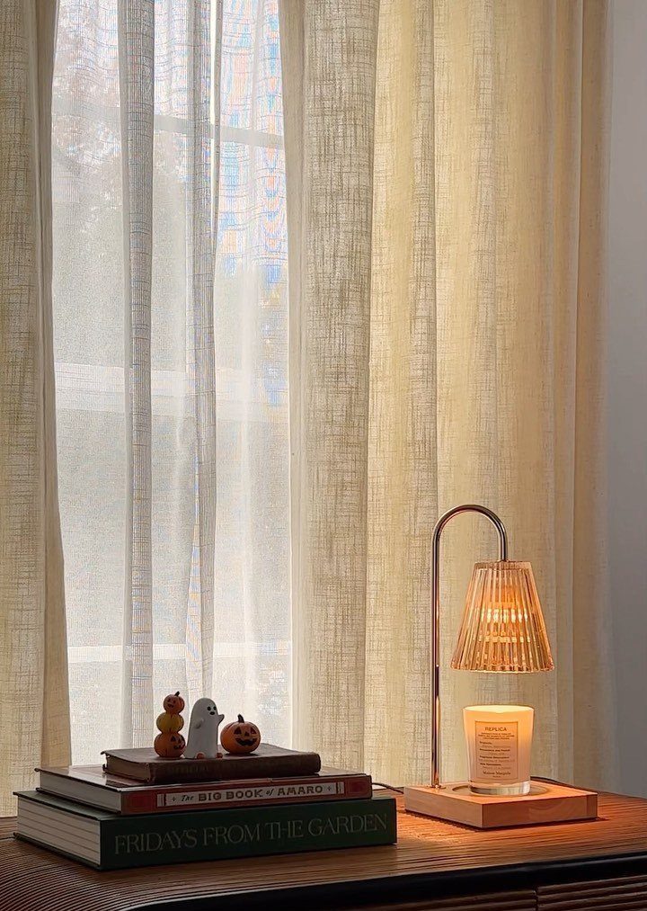 Candle warmer lamp with pleated shade lighting a candle on a wooden table.