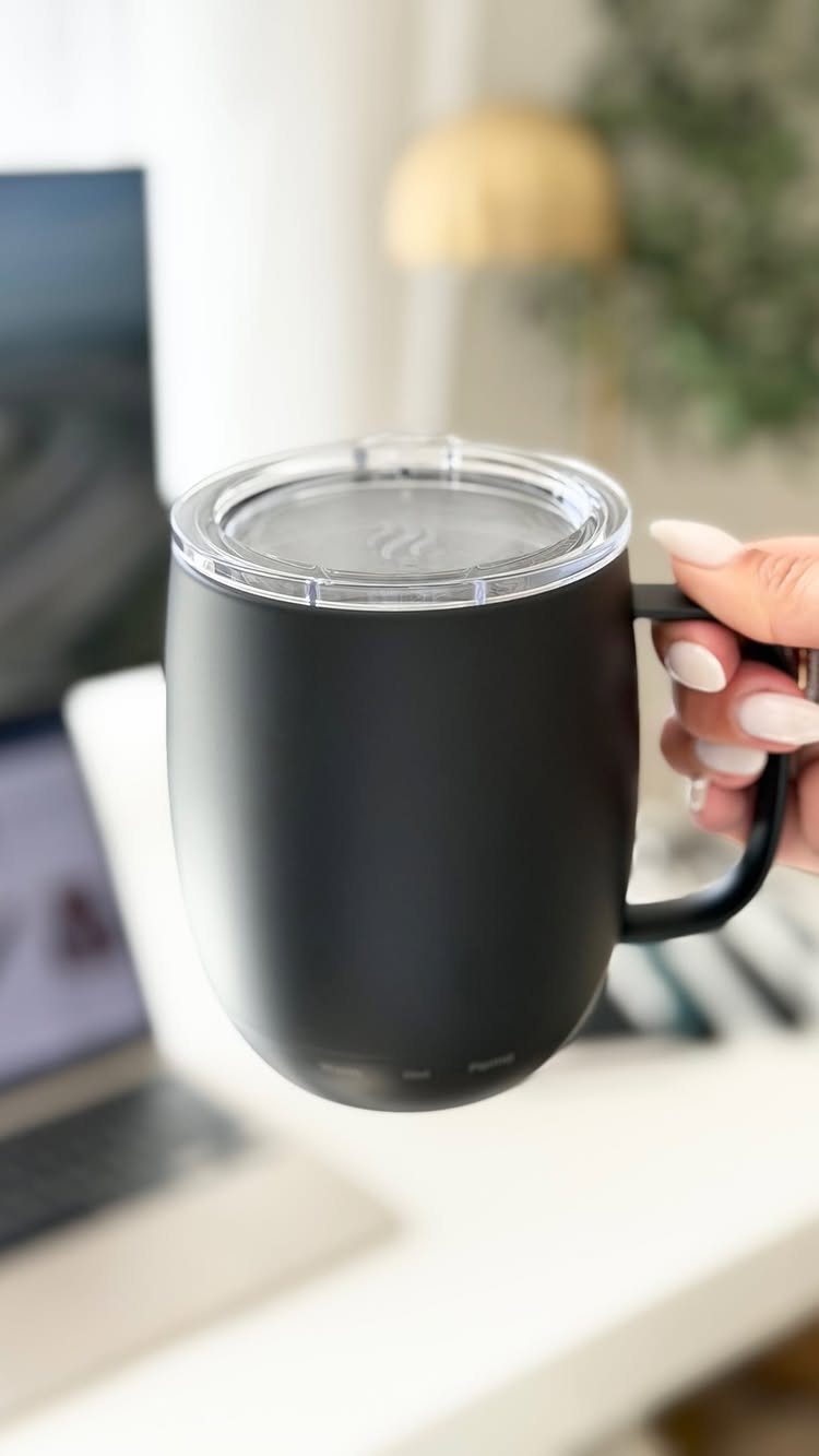 Matte black insulated coffee mug held by a hand over a white desk