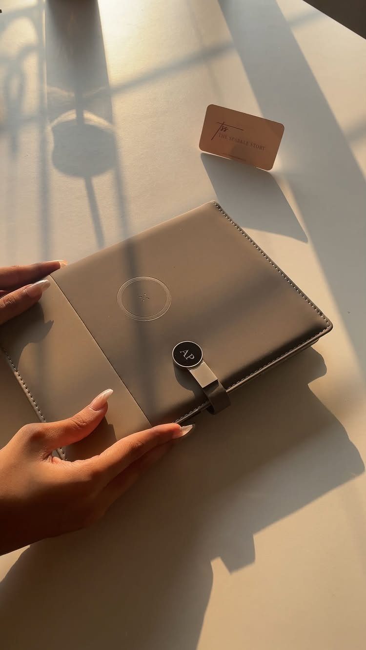Taupe leather tablet case with monogrammed clasp held by hands on white surface