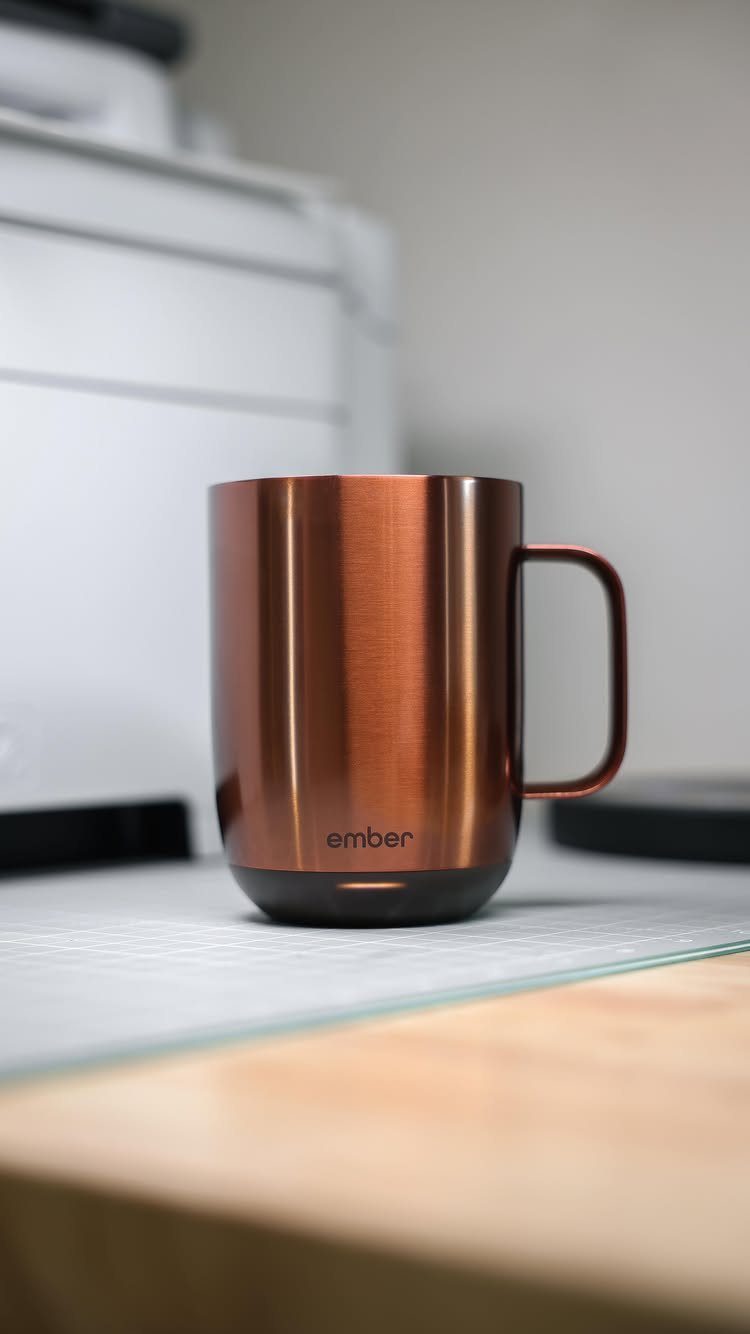 Copper metallic Ember smart mug sitting on a desk in a bright office.