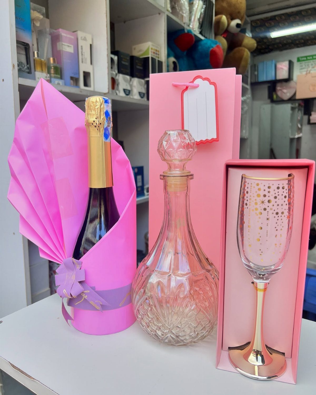 Champagne bottle in pink wrapping with a crystal decanter and gold-rimmed flute.