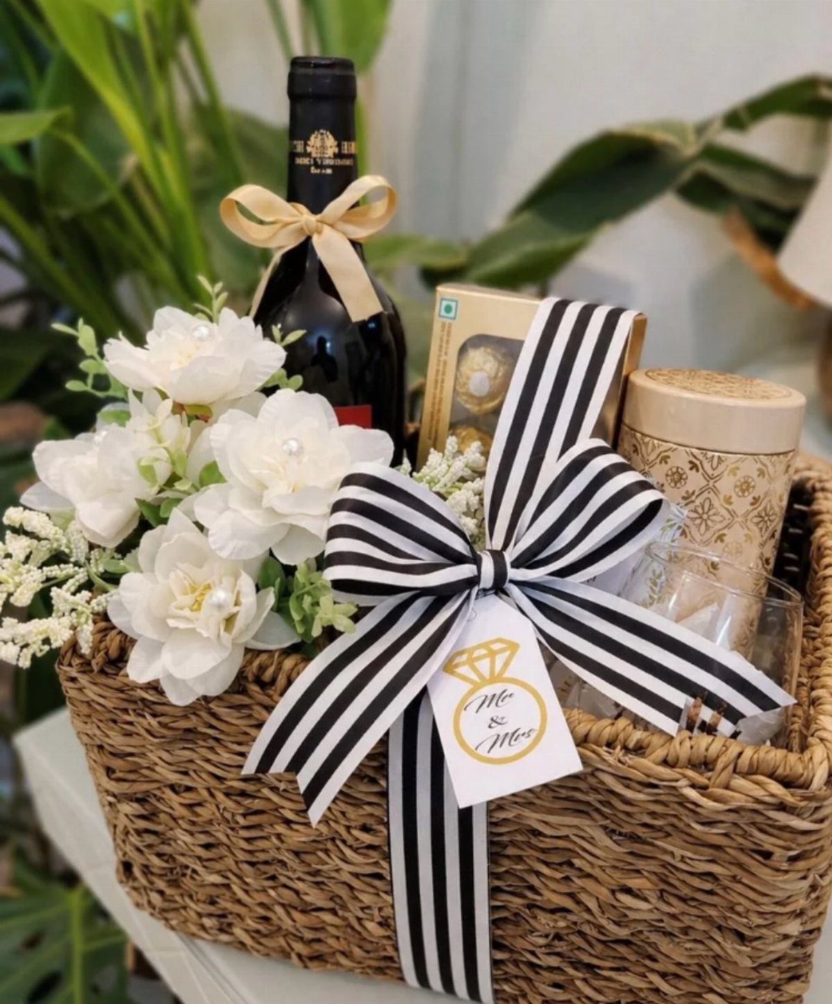 Wine gift basket with red wine, white flowers, and black striped ribbon.