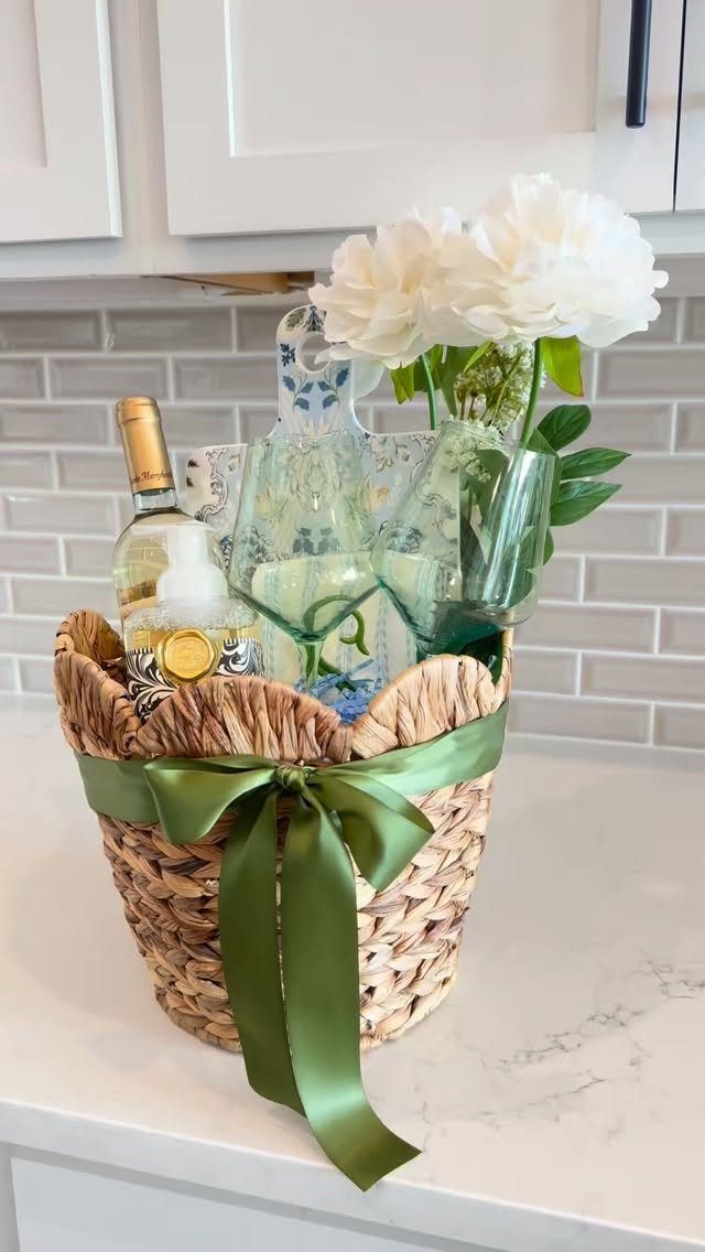 Woven gift basket with white wine, green glasses, and white peonies with green ribbon.