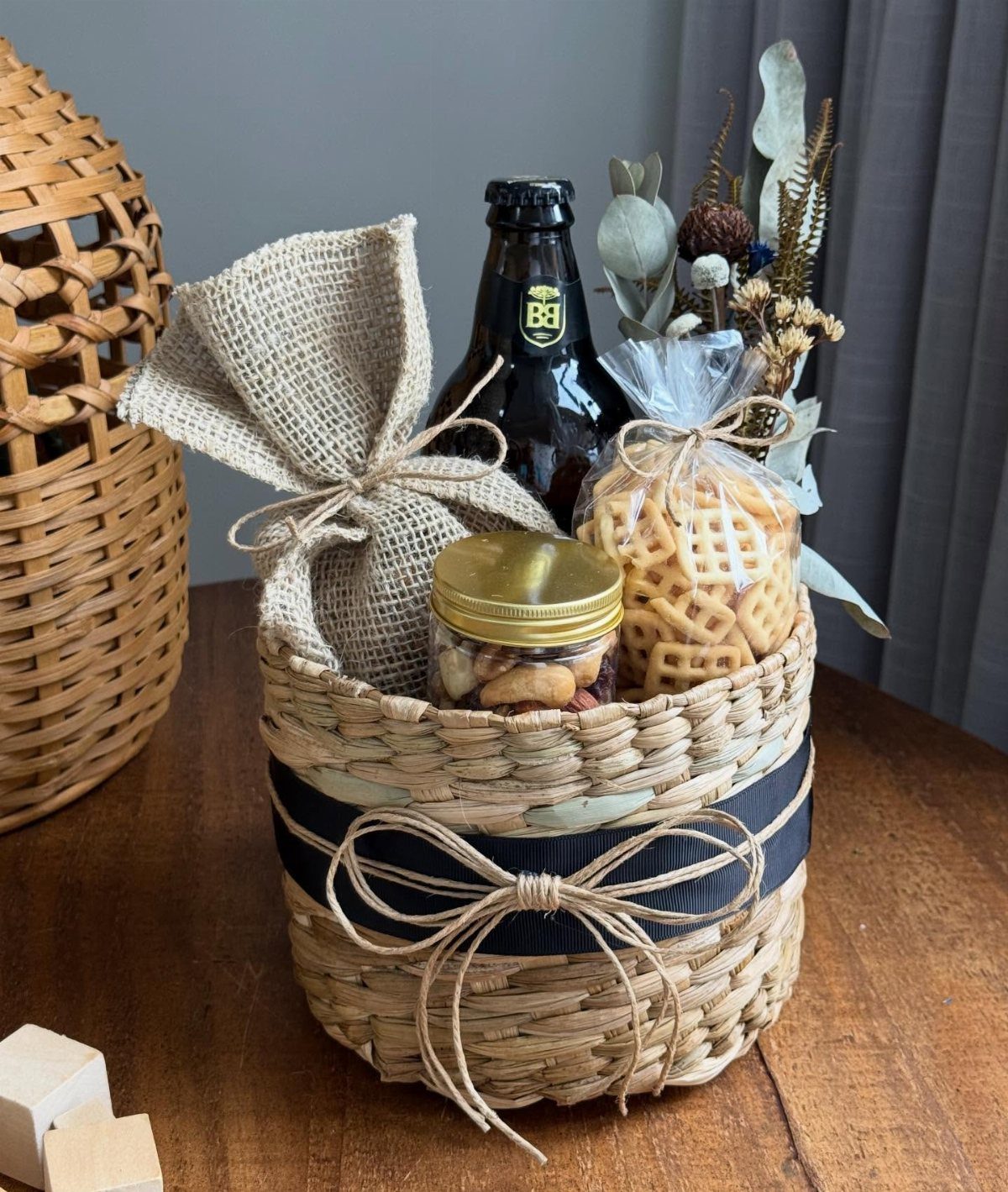 Woven gift basket with a bottle, snacks, and a black ribbon bow.