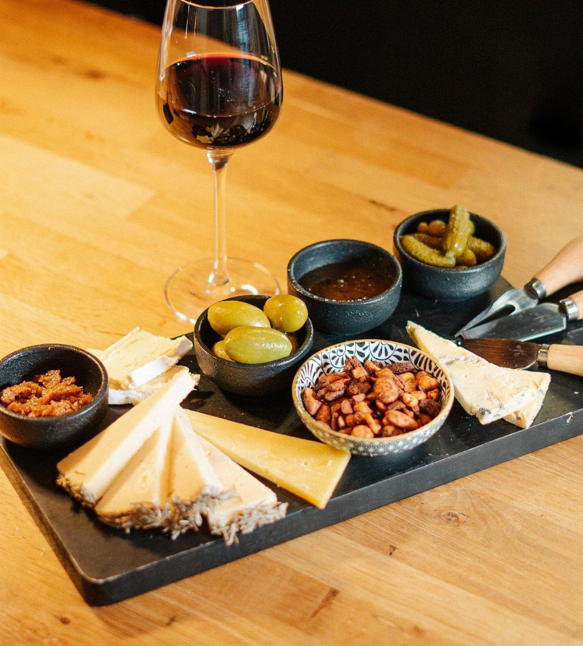 10 Wine Gift Ideas for Every Kind of Wine Lover 9 Cheese board with assorted cheeses, olives, and nuts next to red wine glass.