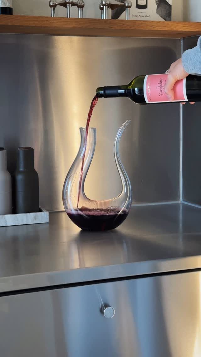 10 Wine Gift Ideas for Every Kind of Wine Lover 2 Red wine being poured from a bottle into a curved glass decanter.